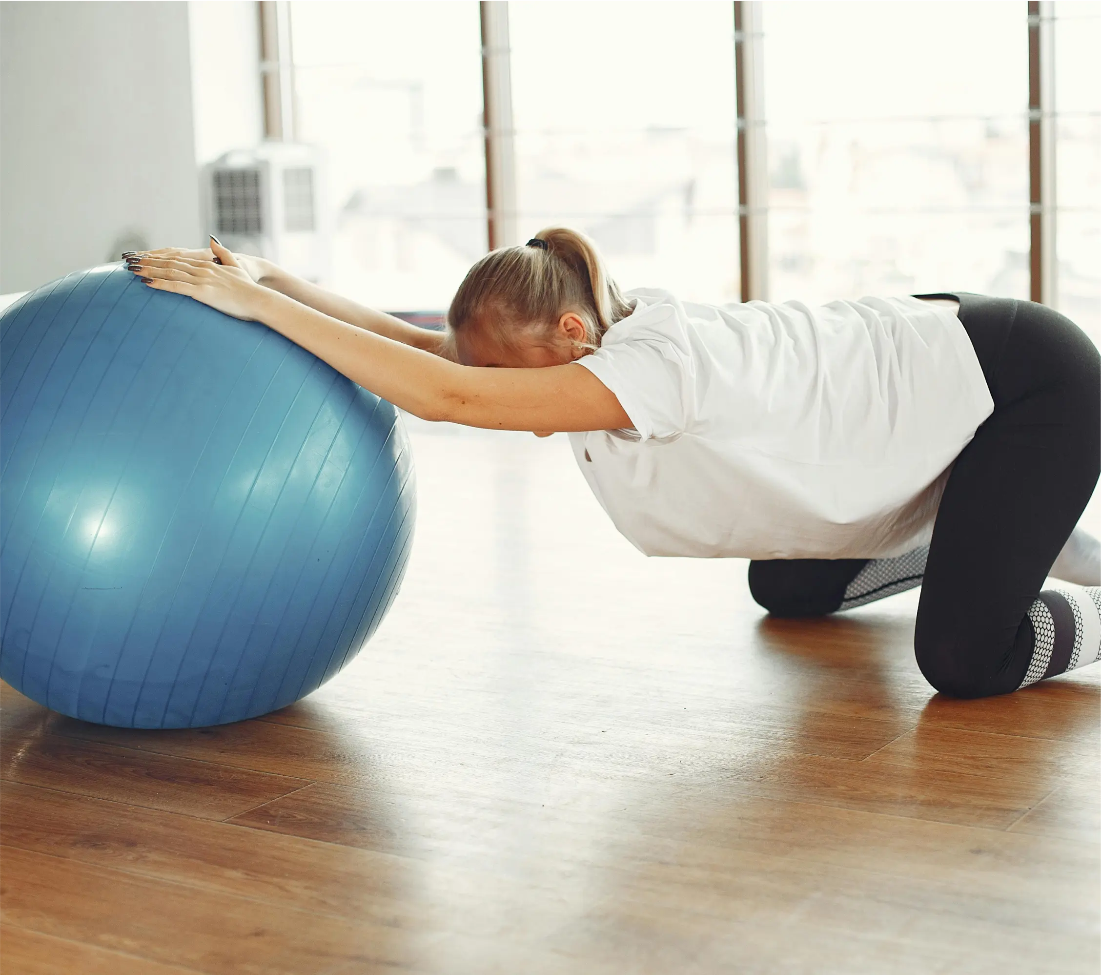 A woman stretching forward with a yoga ball.